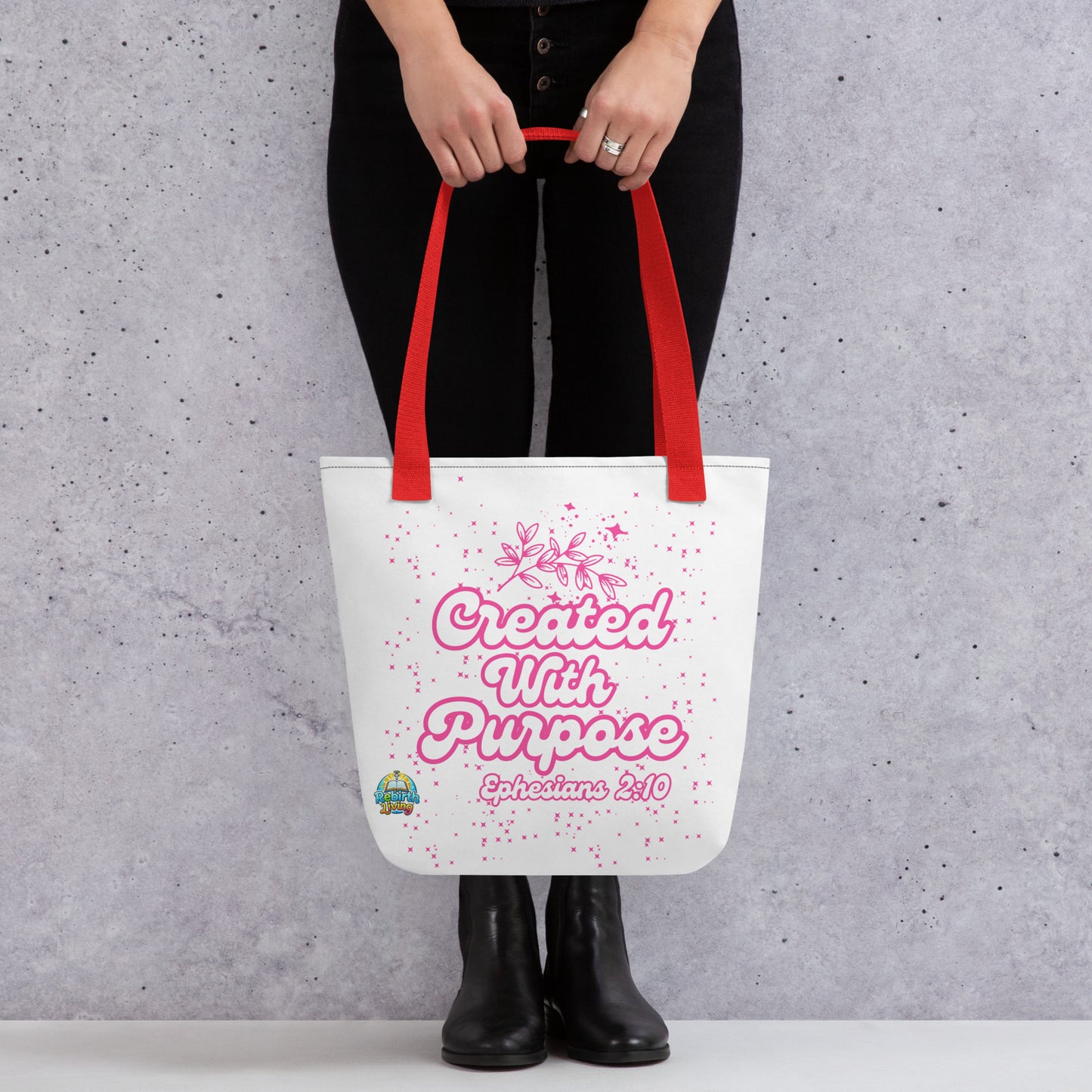 A person holding a Created with Purpose Christian tote bag (15x15) – Ephesians 2:10 KJV scripture design, reusable cotton carryall with a red handle by ReBirth Living