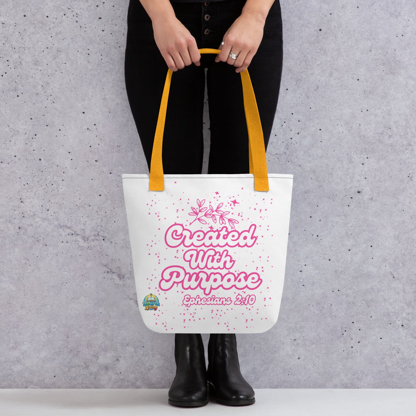 A person holding a Created with Purpose Christian tote bag (15x15) – Ephesians 2:10 KJV scripture design, reusable cotton carryall with a yellow handle by ReBirth Living