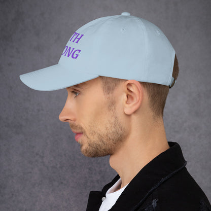 Model is wearing a Faith Strong embroidered hat – bold purple text, light blue adjustable unisex cap by ReBirth Living